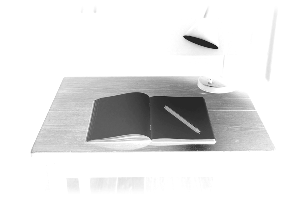 A reading desk at night with an open notebook and a lamp.